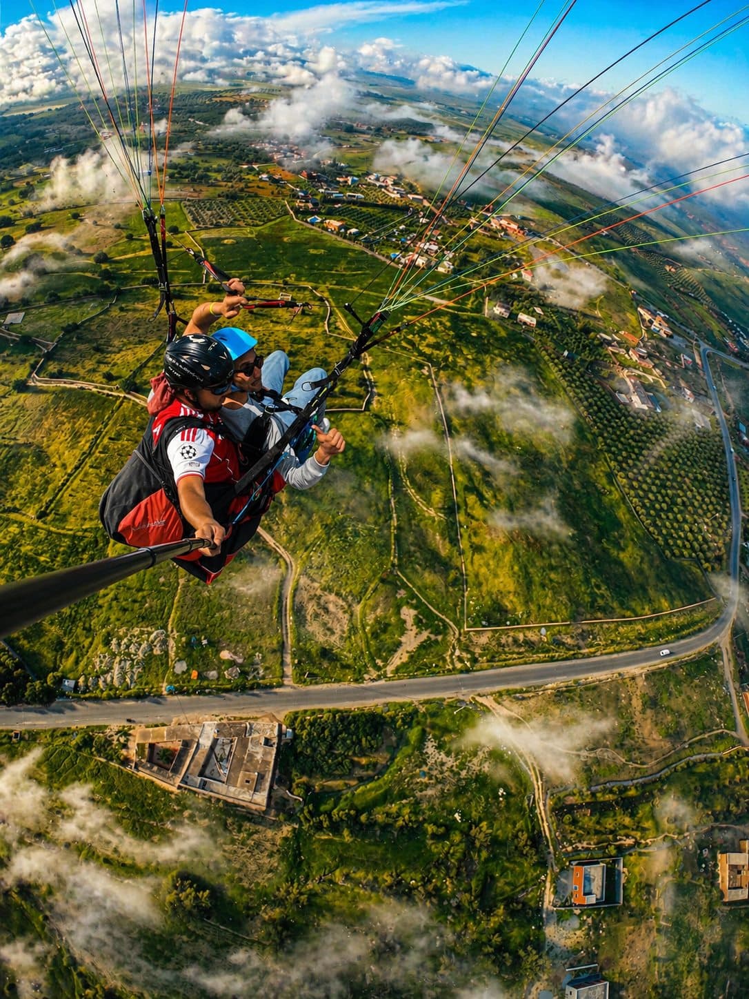 Atlas Paragliding tandem flight soaring above green landscape and low clouds.